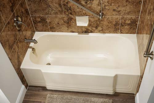 White bathtub with gold tiling on walls.